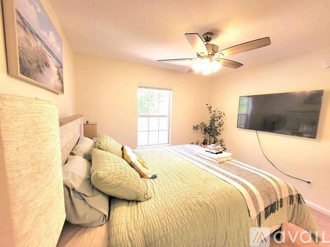 A bedroom with a bed, a ceiling fan, a window, and a painting on the wall.