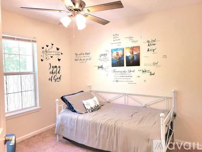 A bedroom with a bed, a ceiling fan, and a wall with pictures and writings.