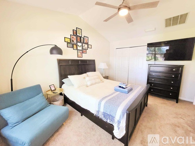 A bedroom with a bed, a blue chair, and a ceiling fan.