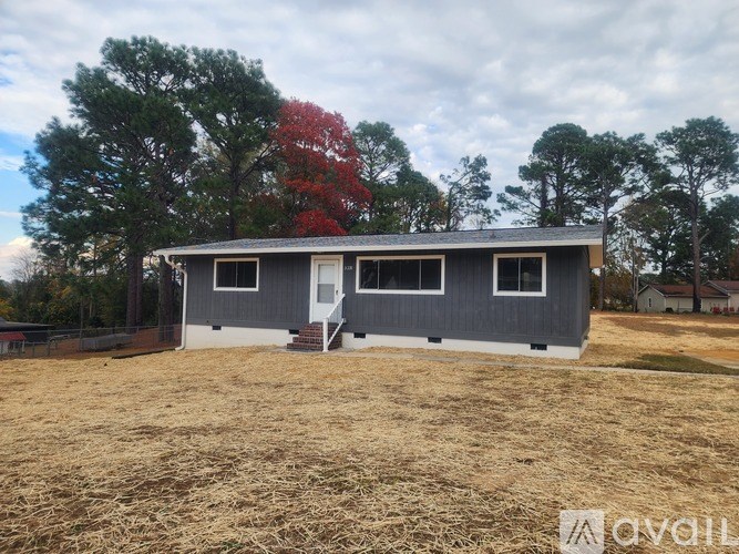 A grey house with a white door and windows is surrounded by a field.