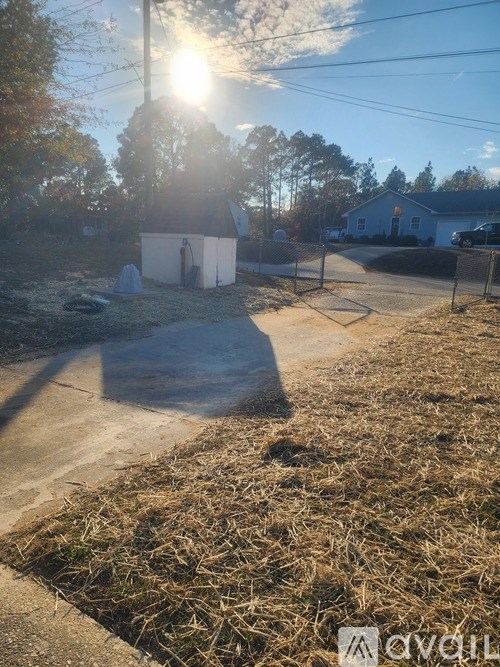 A sunny day in a rural area with a shed and a house in the background.