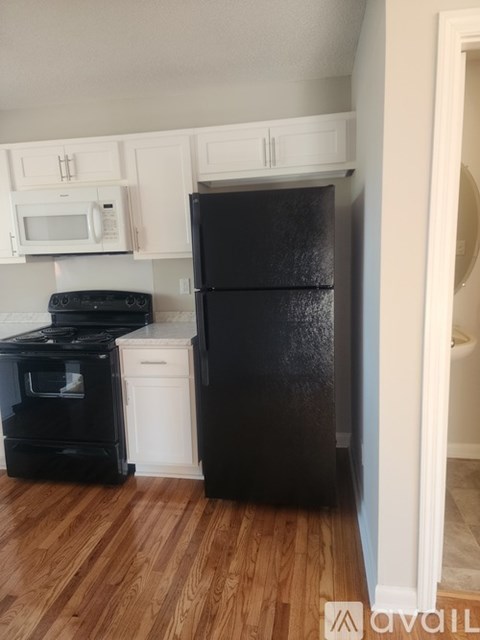 A black refrigerator in a kitchen with wooden floors.