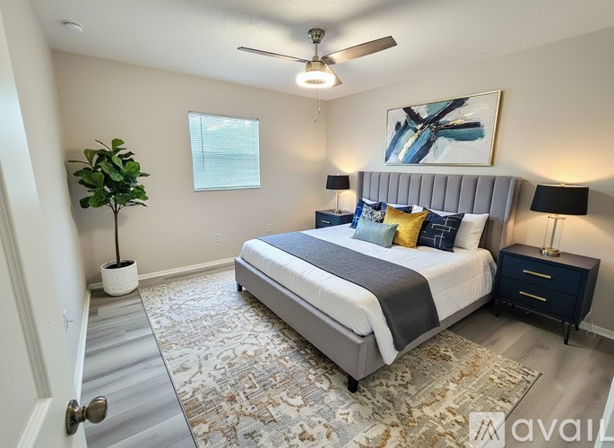 A bedroom with a large bed, a ceiling fan, and a painting on the wall.