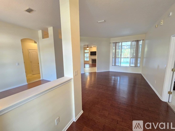 A spacious living room with hardwood floors and a kitchen in the background.