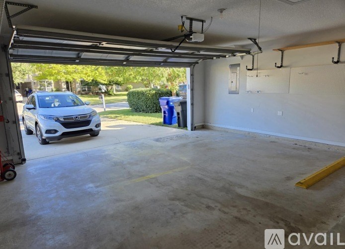 A car is parked in a garage with a blue trash can and a yellow line on the floor.