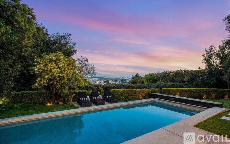 A swimming pool surrounded by a well-manicured garden and lounge chairs.