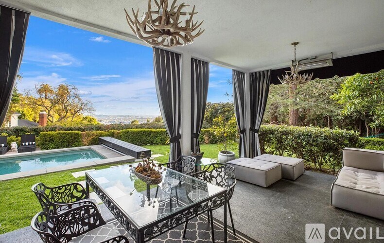 A glass table with a metal frame is in the middle of a patio with a pool and a view of the mountains.