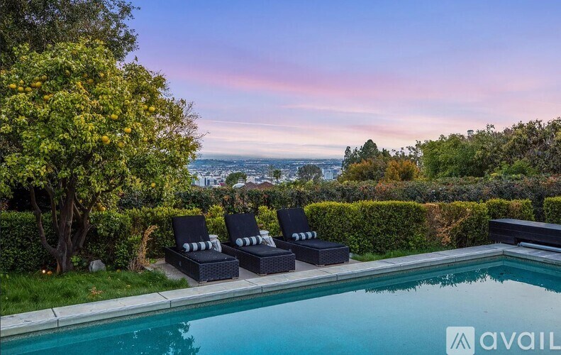 A pool surrounded by black chairs and trees with a view of the city in the background.