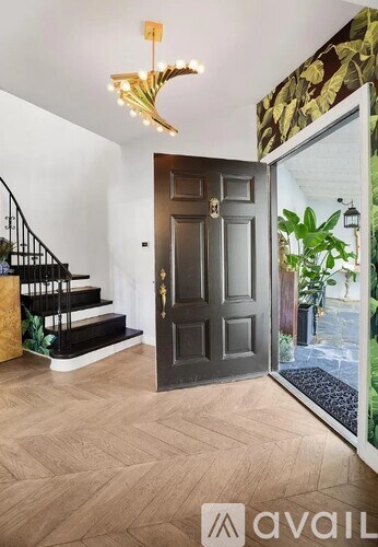 A modern interior with a wooden floor, a staircase with a black railing, and a chandelier.