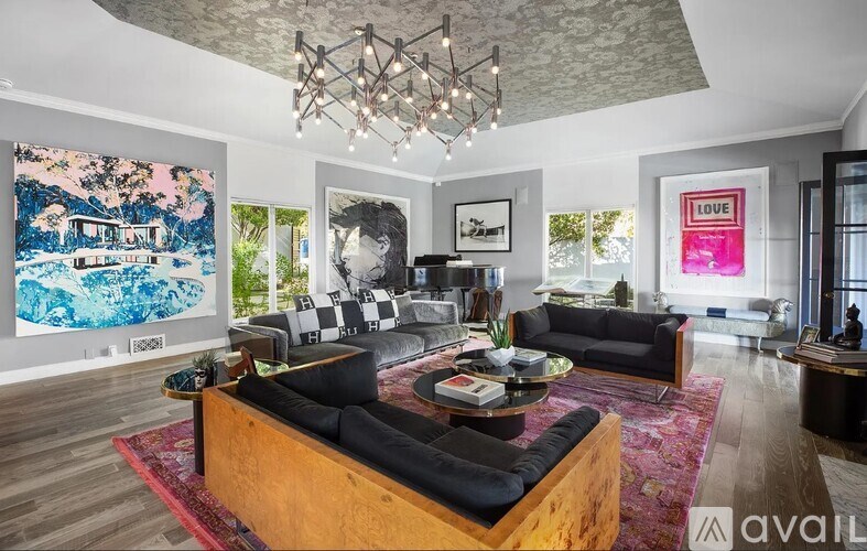 A modern living room with a large painting on the wall and a chandelier hanging from the ceiling.