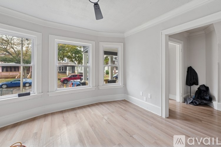 A room with a ceiling fan and a large window with a view of cars and a building outside.