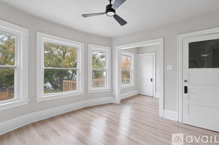 A room with a fan, wooden floors, and a door.