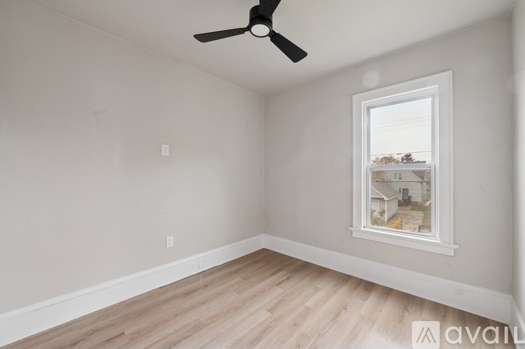 A room with a ceiling fan and a window showing a view of a house.