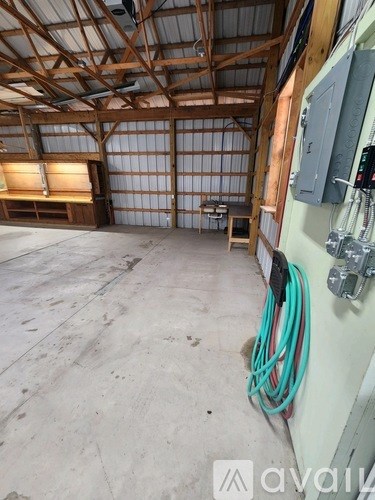 A large empty room with a wooden beam ceiling and a green hose on the wall.