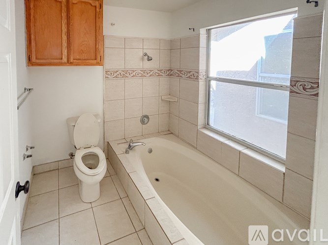 A bathroom with a toilet, tub, and wooden cabinets.