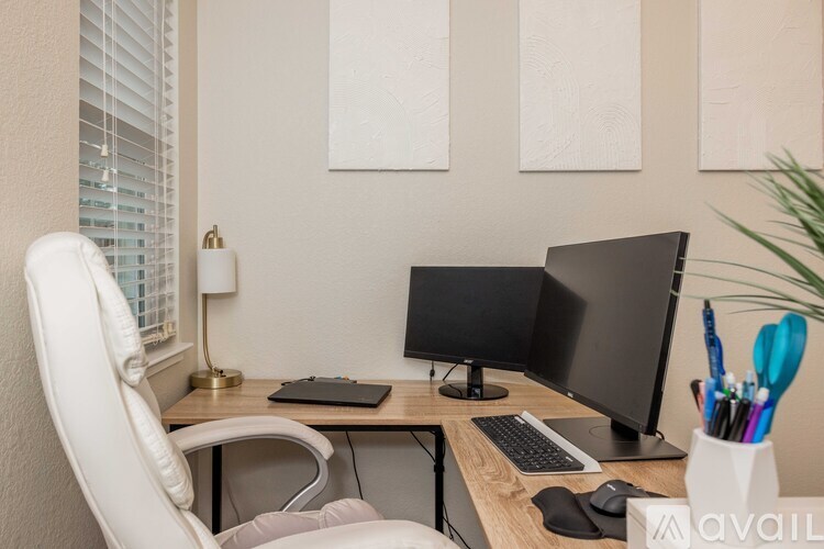 A white chair is in front of a desk with a laptop, a monitor, a keyboard, and a mouse.