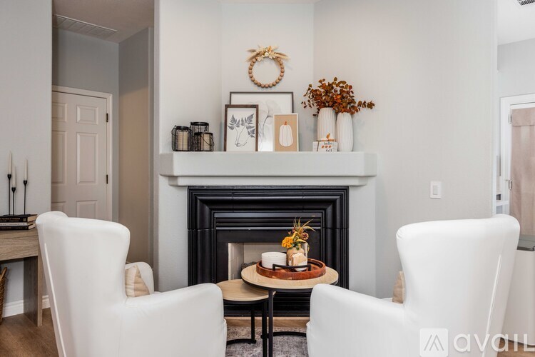 A living room with a fireplace, two chairs and a table with a vase of flowers on it.