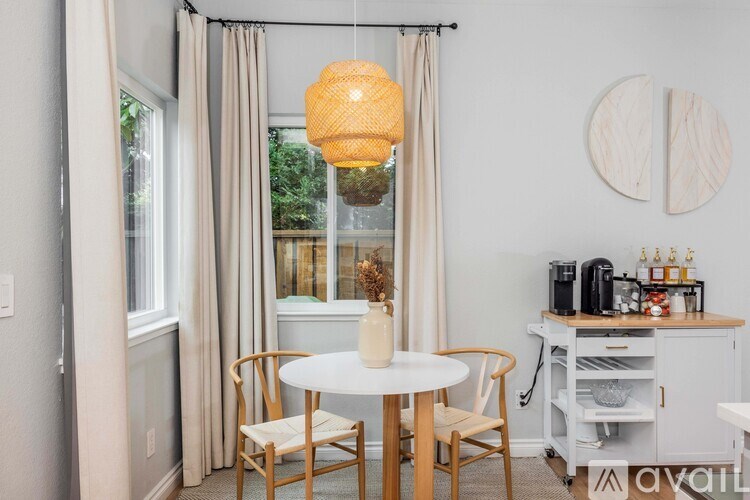 A dining room with a white table and chairs, a hanging light fixture, and a window with curtains.
