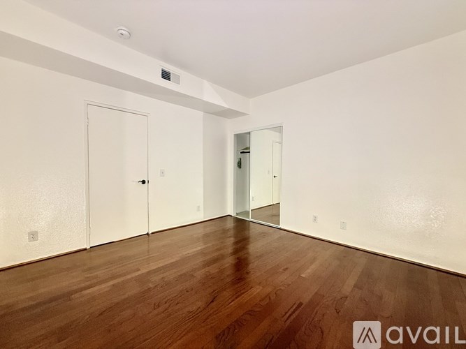 A room with wooden floors and white walls, with a door and a mirror on the wall.