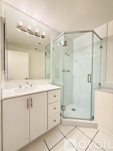 A white bathroom with a glass shower stall and a sink with a mirror above it.