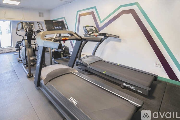 A treadmill with a digital display and a handlebar is in a gym.