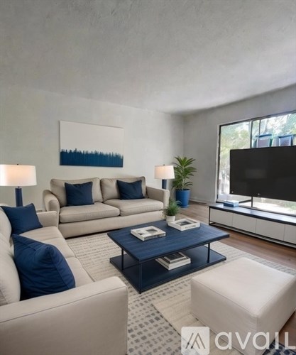 A living room with a white couch, blue pillows, a coffee table, and a flat-screen TV.