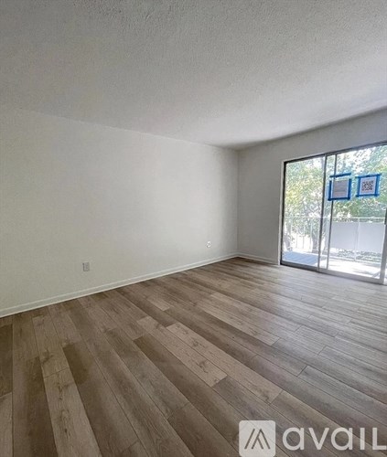 A room with wooden flooring and a window with a view of trees and a building.