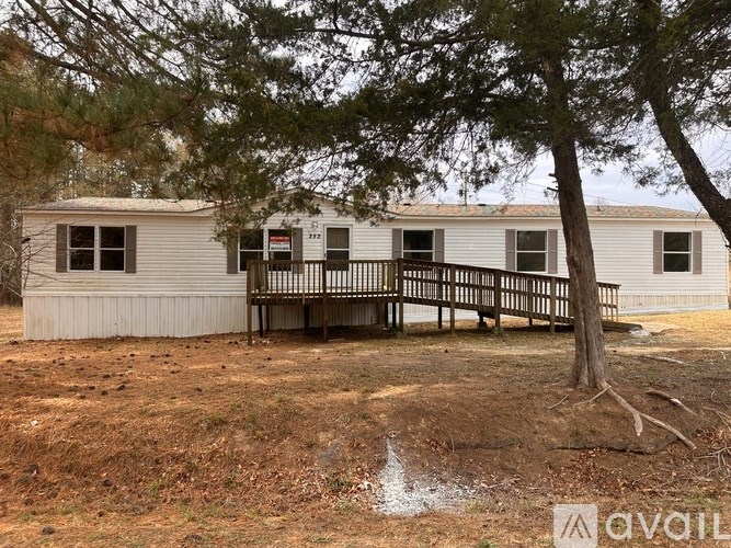 A mobile home with a deck and a tree in front.