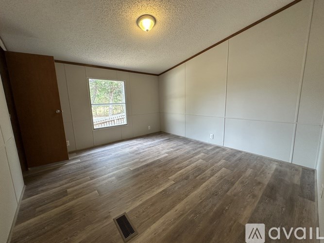 A room with wooden flooring and a window showing greenery outside.