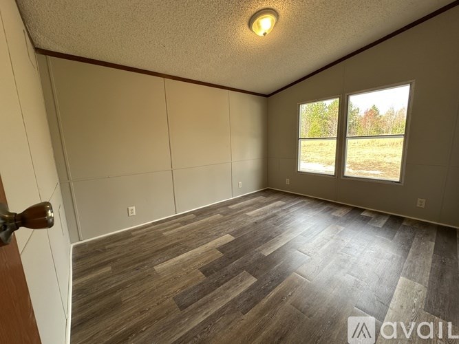 A room with wooden flooring and a window overlooking a grassy area.