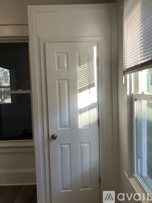A white door with a silver handle is in a room with a window on the right.