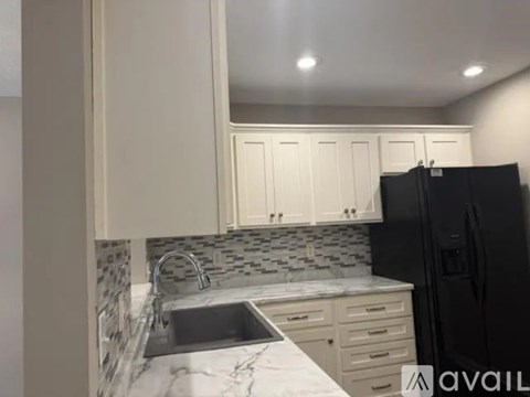 A kitchen with a black fridge, white cabinets, and a marble countertop.