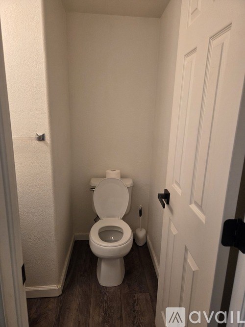 A white toilet in a small bathroom with wood flooring.
