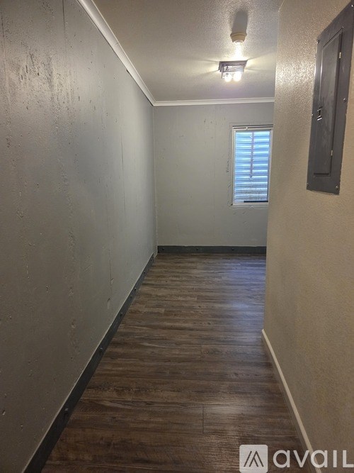 A long, narrow hallway with wood flooring and a window with blinds.