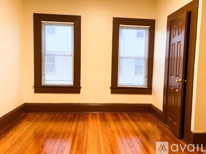 A room with wooden floors and two windows with blinds.