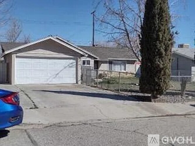 A blue car is parked in front of a house with a garage.