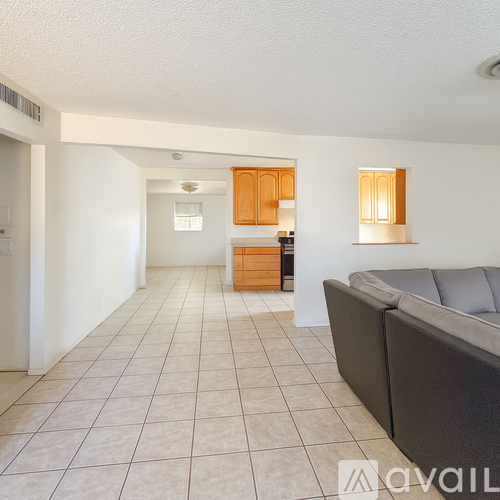 A living room with a grey couch and a kitchen area in the background.