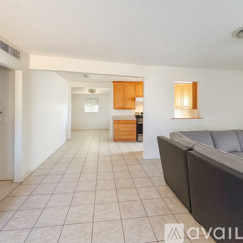 A living room with a grey couch and a kitchen area in the background.