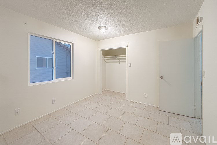 A room with a tiled floor, a window with blinds, and a door leading to another room.