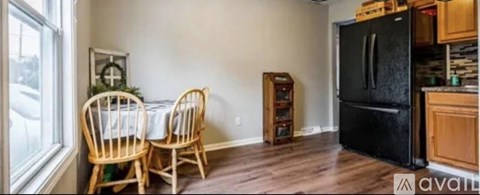 A kitchen with a black fridge, wooden chairs and a dining table.