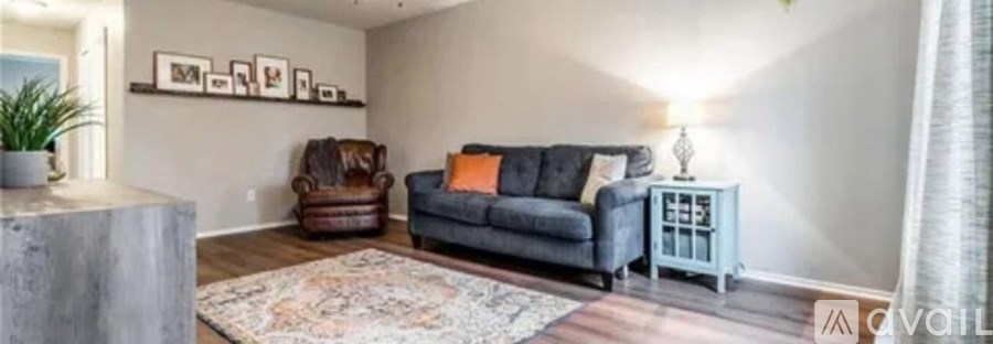 A living room with a grey couch, a brown leather armchair, a wooden side table, and a rug.