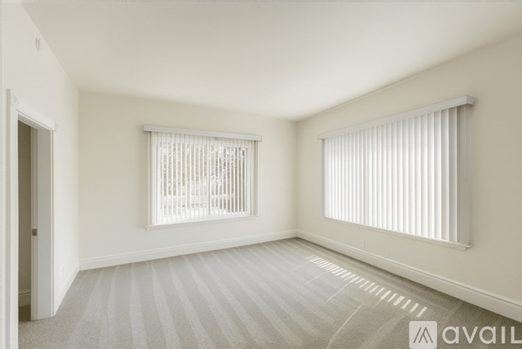 A room with a carpeted floor and two windows with blinds.