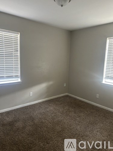 A room with carpeted floor and two windows with blinds.