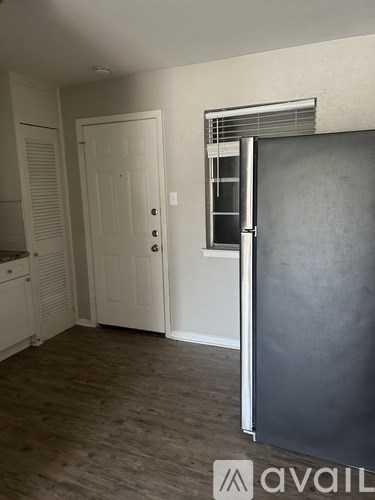 A room with a white door, a window with blinds, and a wooden floor.