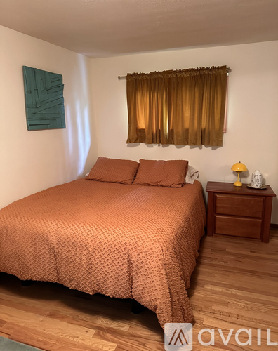 A bedroom with a bed, nightstand, and window with curtains.