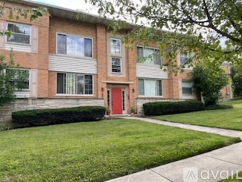 A brick building with a red door and a green lawn in front.
