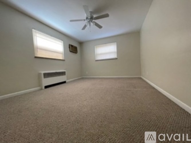 A room with a carpeted floor, a ceiling fan, and a window with blinds.