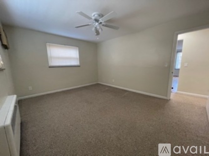 A room with a carpeted floor, a ceiling fan, and a window with blinds.