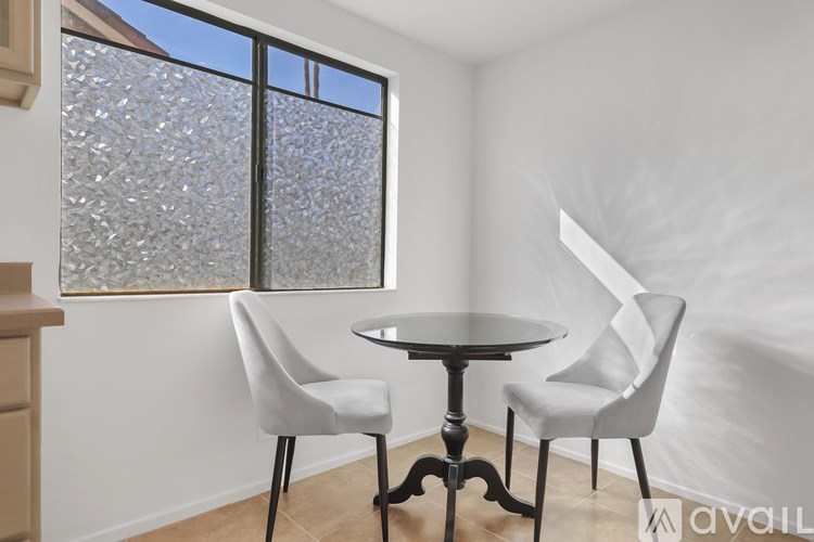 A small table and two chairs are in a white room with a window.
