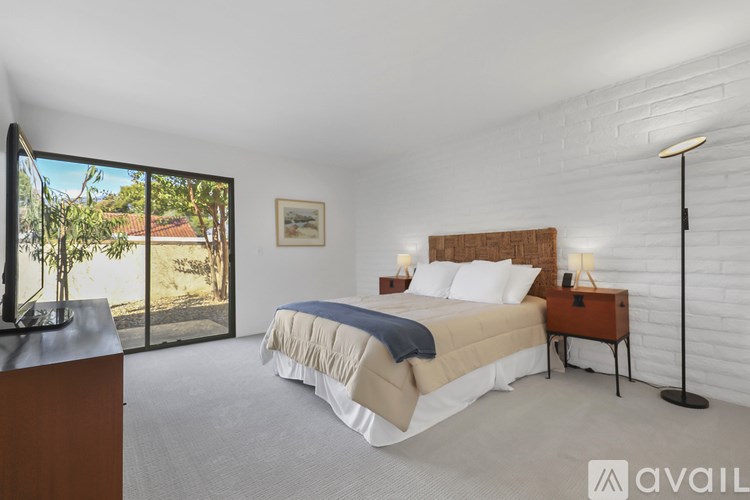 A bedroom with a large bed and a view of the outdoors through a sliding glass door.